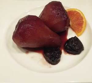 pere al vino servite con prugne e fetta di arancia